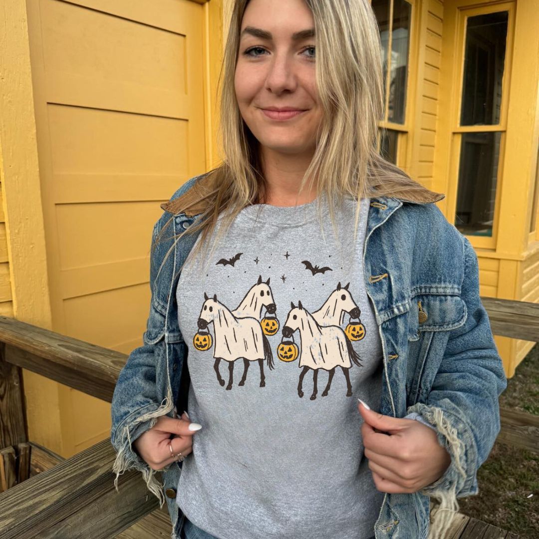 Woman wearing a gray t-shirt with horse illustrations in front of a yellow building.