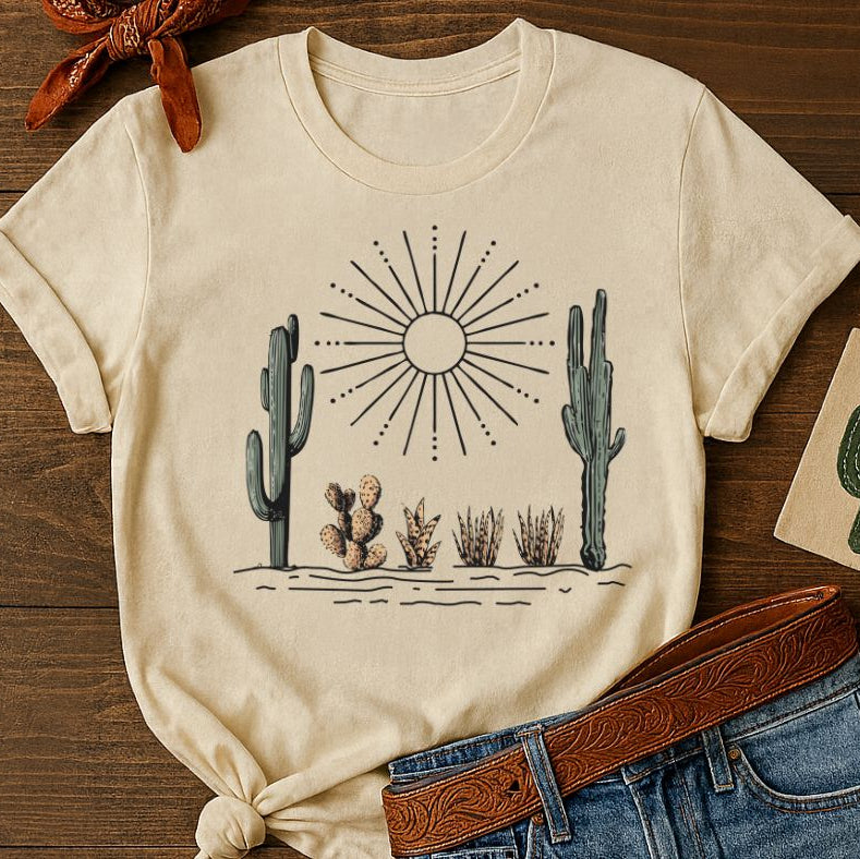 Beige t-shirt with desert scene design on a wooden surface with jeans and belt.