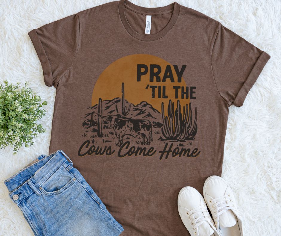 Brown t-shirt with desert graphic and text 'PRAY 'TIL THE COWS COME HOME' on a light background
