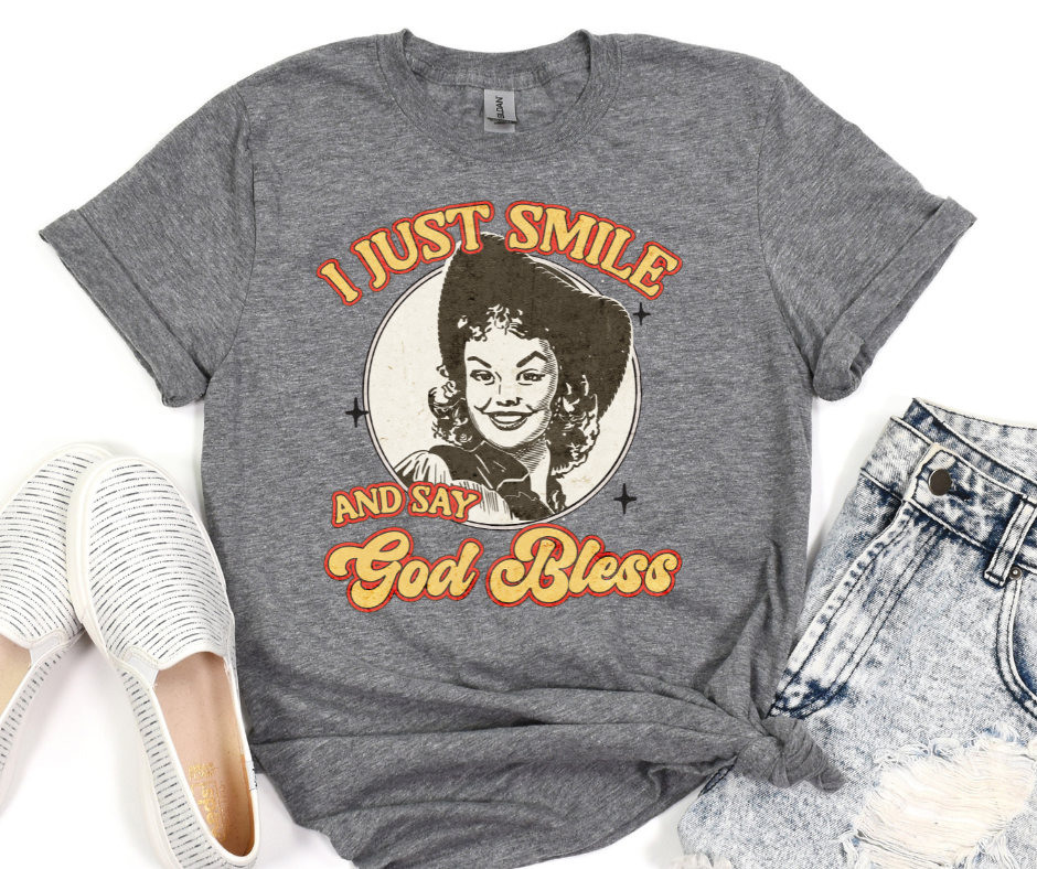 Gray t-shirt with a graphic of a woman and text 'I just smile and say God Bless' on a white background.