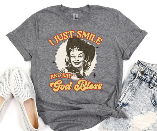 Gray t-shirt with a graphic of a woman and text 'I just smile and say God Bless' on a white background.