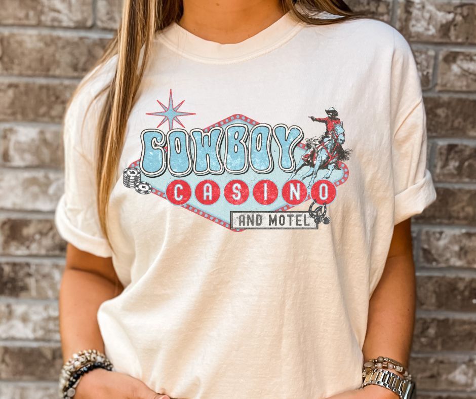 Person wearing a t-shirt with 'Cowboy Casino and Motel' design against a brick wall.