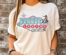 Load image into Gallery viewer, Person wearing a t-shirt with 'Cowboy Casino and Motel' design against a brick wall.
